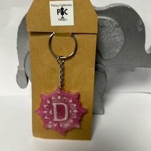 This light pink keychain is crafted in resin with the letter D in the center